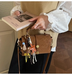 Detalle de bolso bandolera marrón retro con hebilla dorada y colgante de oso pequeño
