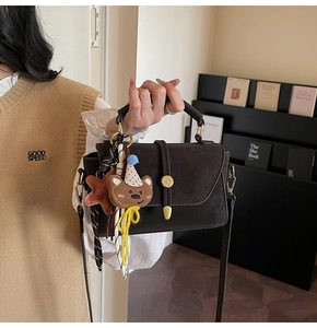 Detalle del bolso de mano marrón oscuro con cierre dorado y colgante de osito