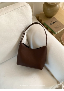Detalle de bolso bucket de cuero marrón oscuro sobre fondo de sofá minimalista