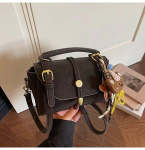 Detalle de bolso retro marrón oscuro con hebilla dorada y colgante de osito