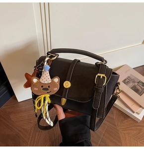 Detalle del bolso vintage de cuero marrón con hebilla dorada y colgante de oso