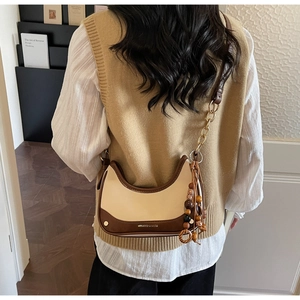 Detail of a chic crescent bag with bicolor leather design and colorful beaded keychain