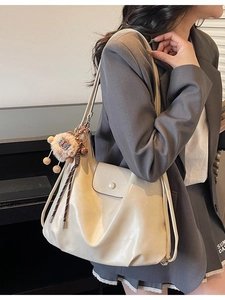 Large beige tote bag with plush charm shown from a side view on a model