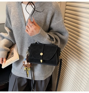 Detalle de bolso negro con cierre circular dorado y colgante de osito marrón