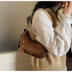 Detail of a brown patchwork half-moon bag with gold chain strap and wooden bead tassel