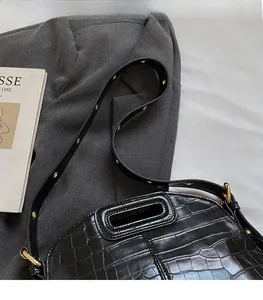 Detail of black crocodile-embossed handbag with gold hardware studs on a blazer