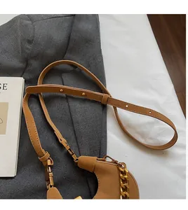 Détail d'un sac demi-lune marron avec chaîne dorée sur une veste grise texturée
