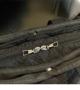 Detail showing smooth silver double metal zippers and quilted diamond pattern on black tote bag