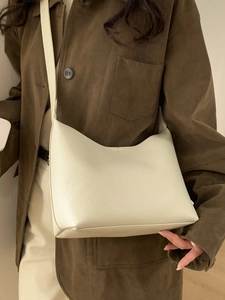 Bolso cubo minimalista en cuero crema llevado al hombro por una modelo elegante