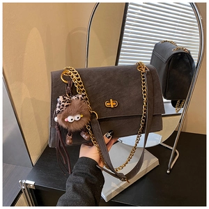 Detail of dark grey retro crossbody bag featuring a gold chain and plush bear charm