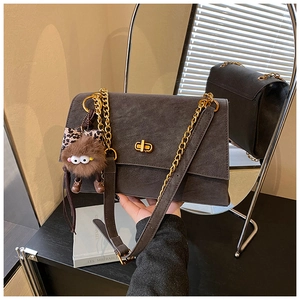 Detail of dark grey suede crossbody bag with gold chain strap and plush leopard charm