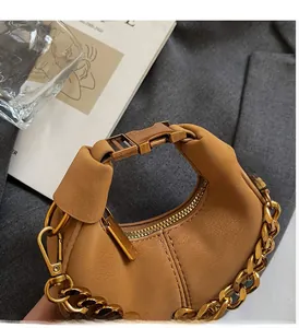 Détail du sac demi-lune en cuir marron avec chaîne dorée sur tissu de costume gris