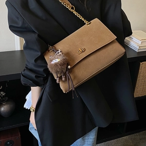 Detail of brown suede tote with gold swivel clasp, chain strap, and cute monster pendant