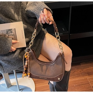 Detail of hobo bag with gold chain strap, bohemian tassel charm and leather texture