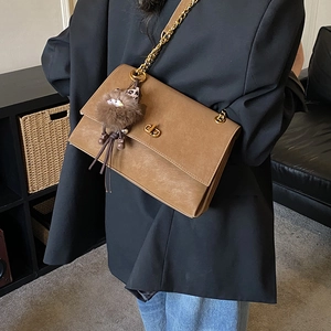 Detailed view of vintage brown crossbody bag with gold chain and plush charm on a model