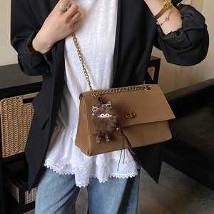 Close-up of retro brown shoulder bag with gold chain strap and plush monster charm detail