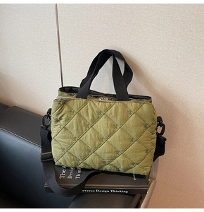 Detail of green quilted tote bag featuring bow embroidery and black nylon straps