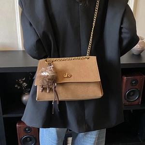 Close-up of vintage tan leather crossbody bag with gold chain strap and plush charm
