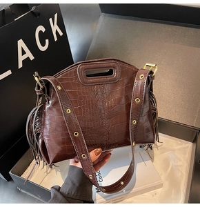 Detail of dark brown crocodile embossed leather bag with side fringe and gold eyelet strap
