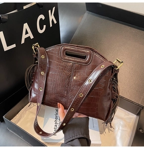 Detail of dark brown crocodile pattern bag with fringe accents and metal eyelet strap