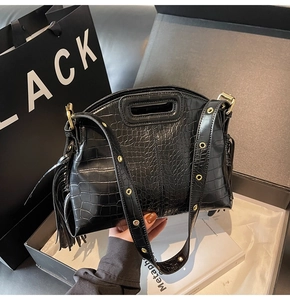 Detail of black crocodile texture shoulder bag with tassel and gold eyelet strap