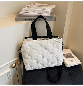 Close-up of white quilted bag with floral embroidery and black woven shoulder straps