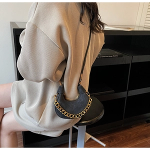 Detail of a black crescent moon bag with premium gold chain and suede texture on a model