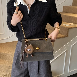 Detail of grey flap crossbody bag with gold lock and leopard print plush monster charm