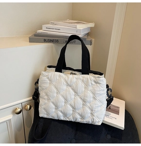 Detail of white quilted bag with floral embroidery and adjustable black shoulder strap