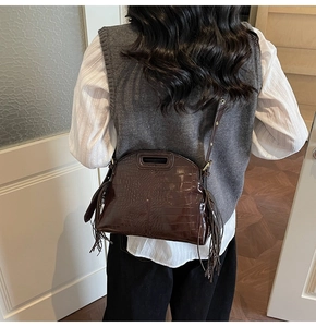 Detail of dark brown croc-effect crossbody bag with tassel and hollow handle on model