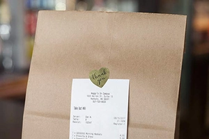 Close-up of heart-shaped gold metallic Thank You sticker sealing a paper gift bag