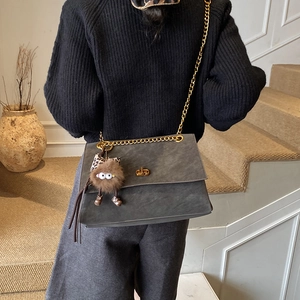 Detail showing grey faux suede flap bag with gold chain strap and plush pendant on model