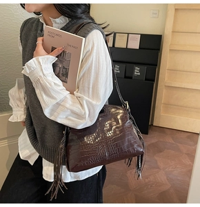 Close-up of a dark brown crocodile-patterned underarm bag with stylish long side tassels