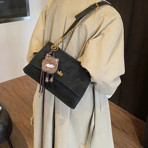 Detail of black suede shoulder bag with gold twist lock and a brown plush monster charm