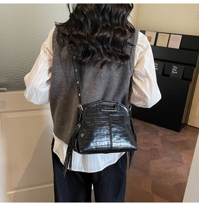 Detail of black crocodile embossed shoulder bag with long side tassels shown in lifestyle use