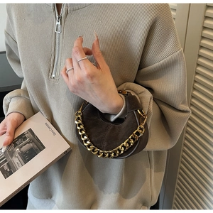 Close-up of brown suede hobo bag with bold gold chain handle held by a model