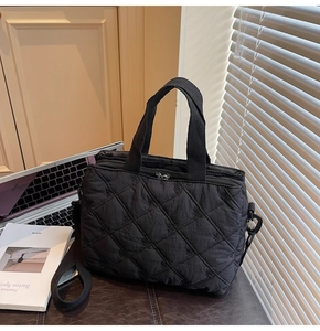 Close-up of black quilted shoulder bag with bow embroidery and adjustable nylon strap