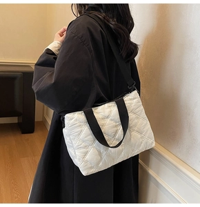 Close-up of a white quilted tote bag featuring a black strap and butterfly embroidery