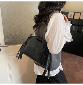 Side view of a black crocodile pattern shoulder bag featuring long fringe and metallic rings