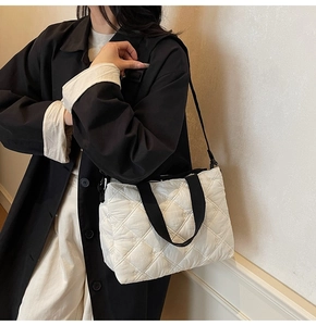 Detail of white quilted tote bag with black straps and adjustable shoulder belt