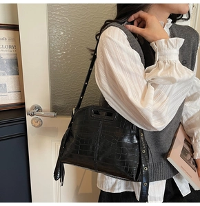 Close-up of black crocodile embossed shoulder bag with gold metal eyelets and top handle