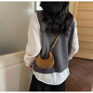 Detail view of brown half-moon crossbody bag with gold chain strap worn by a model