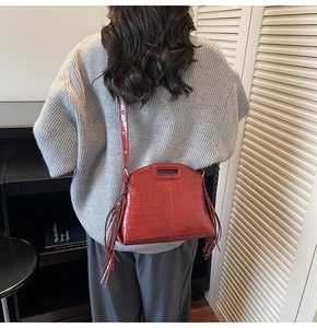 Detail of red crocodile pattern shoulder bag with side tassels on a casual model