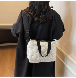 Detailed view of white quilted tote bag with black straps worn over a long black coat