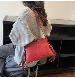 Detail of burgundy crocodile-embossed bag with long fringe and metal grommet strap