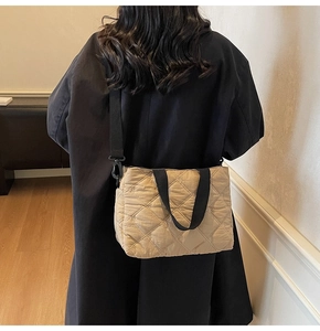 Beige quilted tote bag with black straps worn by a model in a minimal room setting