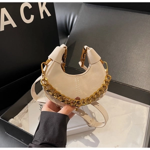 Detail of cream crescent leather handbag featuring a chunky gold chain and vertical stitching