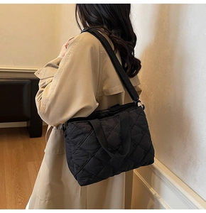 Detail of black quilted shoulder bag with diamond stitching and adjustable strap on a model