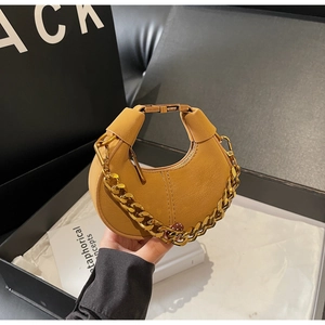 Close-up of mustard yellow leather moon bag with decorative thick gold chain and top handle