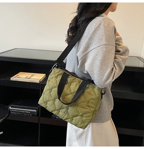 Detail of light green quilted tote bag featuring small floral embroidery and black straps